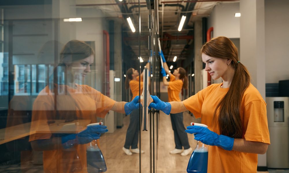 Two young employees cleaning company clean mirrored surfaces coworking space
